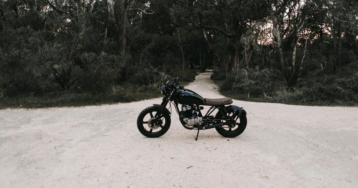 Zwarte motor geparkeerd op een zandweg in een bos