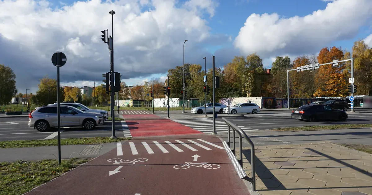 Een rood fietspad met witte pijlen en fietssymbolen bij een kruispunt met verkeerslichten